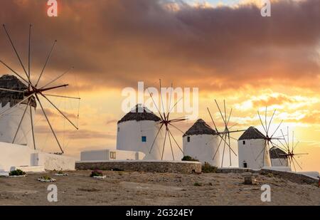 Mulini a vento tradizionali, isola di Mykonos punto di riferimento al tramonto, Cicladi Grecia. Arancio colori cielo nuvoloso sfondo. Destinazione delle vacanze estive Foto Stock