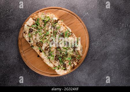 Pinsa romana italiana con lumache d'uva escargata francese su sfondo scuro. Pinsa con lumaca, formaggio, microgredi. Cucina gourmet Italiana. Foto Stock