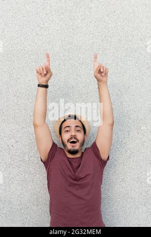 Felice giovane uomo che punta verso l'alto con entrambe le braccia Foto Stock