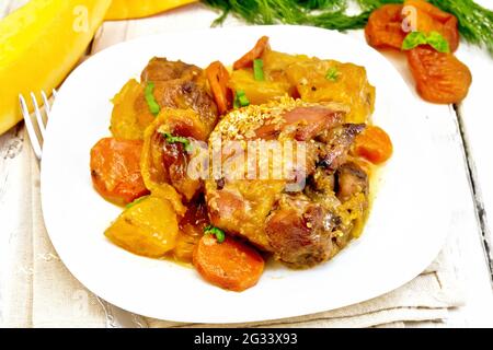 Stufato di pollo con zucca, albicocche secche, carote e vino rosso, cosparso di semi di sesamo in un piatto su un asciugamano da cucina contro tavola di legno Foto Stock