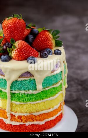 Primo piano di pan di Spagna arcobaleno decorato con frutti di bosco freschi. Foto Stock