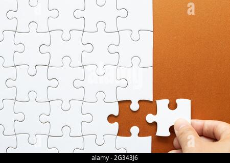 Set di pezzi di puzzle bianchi e mano che tiene ultimo pezzo Foto Stock