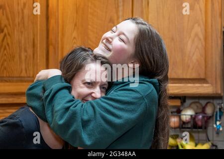 la madre di 42 anni e la sua figlia di 15 anni abbracciano giocosamente, con la figlia che dice è più alta di sua madre ora. (SIG.) Foto Stock