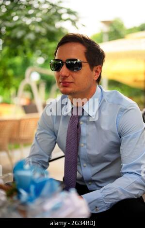Un bell'uomo vestito formalmente seduto in un caffè Foto Stock