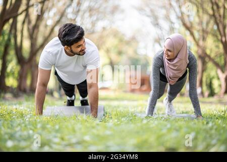 Giovane uomo musulmano e donna in hijab e activewear in piedi in posizione a tavola nel verde parco estivo. Sport e fitness all'aria aperta. Foto Stock