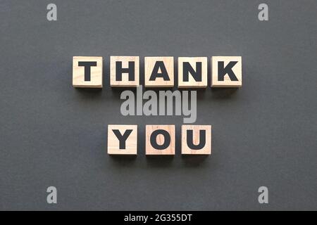 Grazie lettere alfabetiche su blocchi di legno su sfondo grigio scuro. Vista dall'alto. Foto Stock