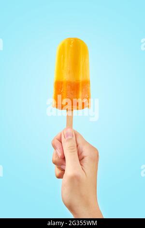 Donna tiene il gelato giallo su sfondo blu. Colore popsicle di frutta surgelata. Foto Stock