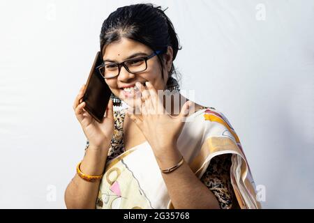 Una bella donna indiana in saree che parla di smartphone e sorridente isolato su sfondo bianco Foto Stock