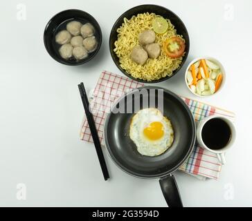 Noodle calde servite con uova e pomodori freschi con polpette su una ciotola nera e sottaceto su una ciotola bianca e uova su fondo bianco Foto Stock