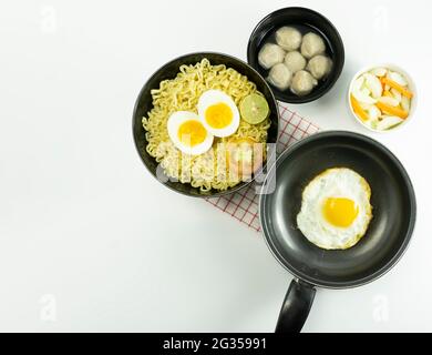 Noodle calde servite con uova e pomodori freschi con polpette su una ciotola nera e sottaceto su una ciotola bianca e uova su fondo bianco Foto Stock