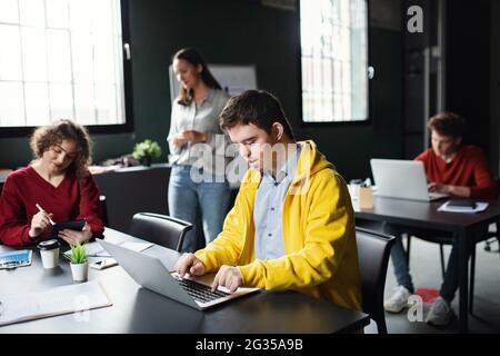 Uomo con sindrome da Down con computer portatile che frequenta la classe di istruzione nel centro della comunità, inclusività di persone disabili. Foto Stock