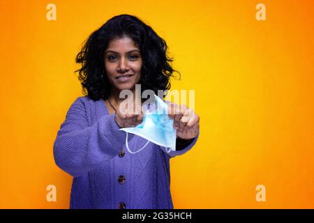 Bella giovane donna indiana strappa la sua covid 19 maschera di protezione - Pretty Sri Lanka ragazza felice per la fine di la canna fumaria pandemica strigge la maschera del virus Foto Stock