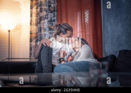 All'interno della casa coppia tiro seduta sul divano rilassante e impasti - giallo e blu atmosfera tono di luce amanti girato parlare in bella casa Foto Stock