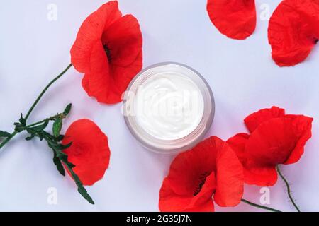 Fiori di papavero e vasetto bianco crema cosmetica. Concetto di cosmetici naturali biologici fatti a mano. Vista dall'alto, disposizione piatta. Foto Stock