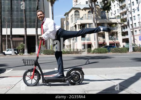 uomo felice uomo d'affari che guida elettro scooter su sfondo urbano, noleggio di trasporto. Foto Stock