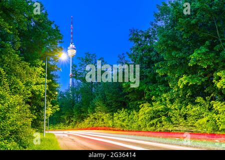 Germania, Stuttgart paesaggio urbano di illuminated la torre della televisione che costruisce le luci e la strada di traffico in paesaggio verde della natura degli alberi di notte Foto Stock