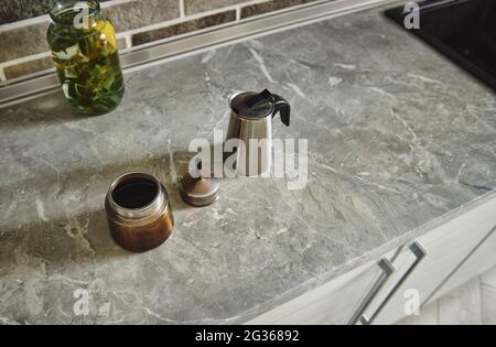 Vista ad alto angolo di una macchina da caffè geyser in acciaio smontata accanto a una bottiglia di vetro di acqua alla menta-limone sul piano cucina. Foto Stock