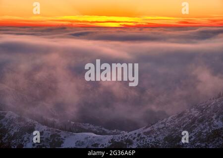 Atmosfera magica di un tramonto nelle alture; nuvole al tramonto su creste di montagna innevate Foto Stock