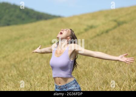 Donna eccitata urlando in un campo di grano che allunga le braccia Foto Stock