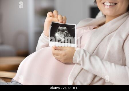 Primo piano di una donna incinta sorridente che mostra un'immagine ecografica Foto Stock