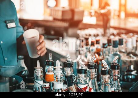 Barista che mette il ices in vetro e preparando un fresco, gustoso mix di coctail estivo sul bancone bar. Molte bottiglie sfocate e macchina per la birra sul bac Foto Stock