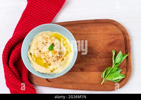 Hummus, purè di ceci con limone, spezie ed erbe su una ciotola sopra un tavolo di legno. Foto Stock