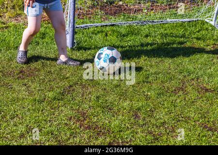 Vista ravvicinata dei piedi del bambino vicino alla palla sullo sfondo del prato erboso. Foto Stock