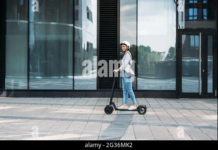 Giovane uomo d'affari che indossa il casco da ciclismo che guida spinga lo scooter sul sentiero Foto Stock