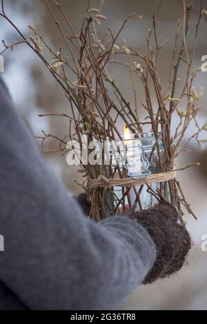 lanterna portata, un vetro è decorato dall'esterno con bastoni, ramoscelli, ramoscelli. Una candela si alza e brucia nel vetro, al riparo dal vento, Foto Stock