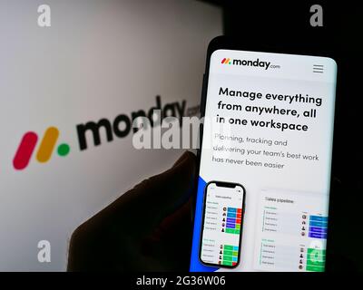 Persona che tiene il cellulare con la pagina web della società software israeliana Monday.com Ltd. Sullo schermo davanti al logo. Mettere a fuoco il centro del display del telefono. Foto Stock