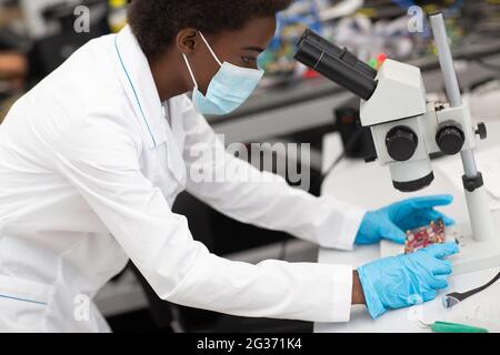 Scienziata afroamericana lavora in laboratorio al microscopio. Donna a colori nella tecnologia. Foto Stock