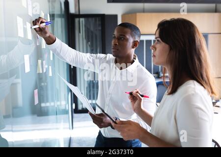 Uomo d'affari e donna d'affari diversi che scrivono su appunti su tavola di vetro in ufficio moderno Foto Stock