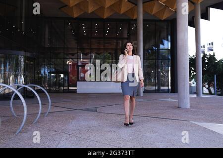 Donna d'affari caucasica che parla con uno smartphone mentre si cammina nel parco aziendale Foto Stock