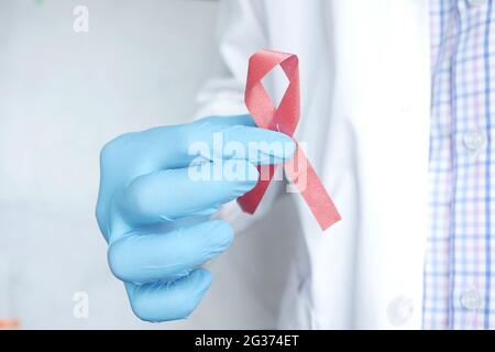 Mano del medico che tiene in primo piano il nastro di HIV di colore rosa Foto Stock