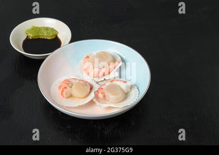 Capesante grezzo naturale con gamberi bolliti nel lavandino in una ciotola di ceramica con salsa di soia e wasabi su fondo scuro. Messa a fuoco selettiva. Foto Stock