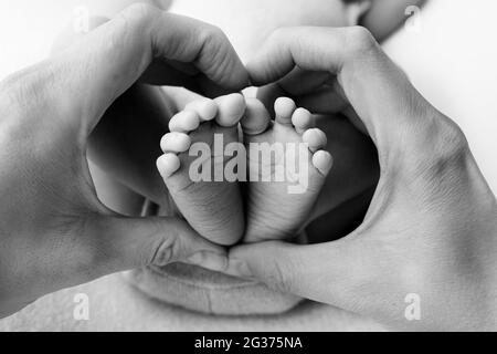 Le mani di un genitore a forma di cuore intorno ai piedi di un neonato. Primo piano dei piedi del bambino a forma di cuore nelle mani. Foto Stock