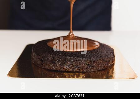 Lo chef versa ganache sulla torta al cioccolato. Foto Stock