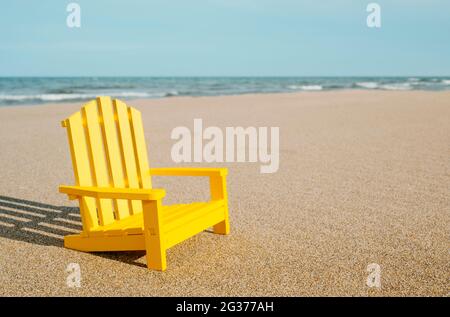 primo piano di una sedia in miniatura gialla sulla sabbia di una spiaggia solitaria, con il mare sullo sfondo Foto Stock