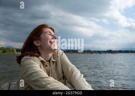 Giovane donna che si allunga felicemente, sul lago, Starnberger See, alta Baviera, Baviera, Germania Foto Stock