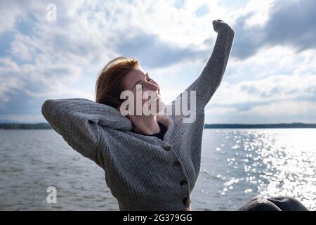 Giovane donna che si allunga felicemente, sul lago, Starnberger See, alta Baviera, Baviera, Germania Foto Stock