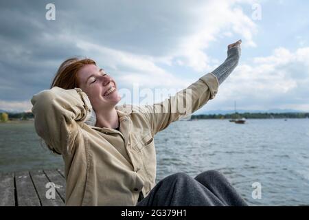 Giovane donna che si allunga felicemente, sul lago, Starnberger See, alta Baviera, Baviera, Germania Foto Stock