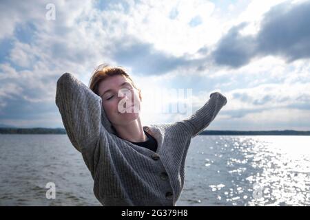 Giovane donna che si allunga felicemente, sul lago, Starnberger See, alta Baviera, Baviera, Germania Foto Stock