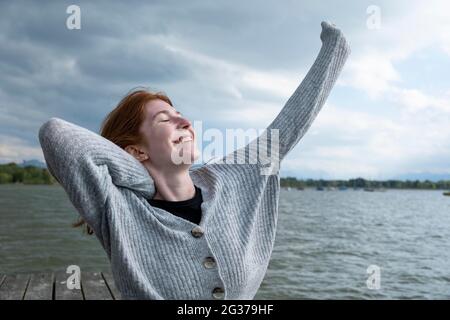 Giovane donna che si allunga felicemente, sul lago, Starnberger See, alta Baviera, Baviera, Germania Foto Stock