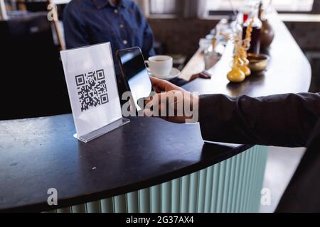 Sezione centrale dell'uomo che effettua un pagamento tramite la scansione del codice qr dallo smartphone in un bar Foto Stock