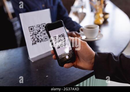 Sezione centrale dell'uomo che effettua un pagamento tramite la scansione del codice qr dallo smartphone in un bar Foto Stock