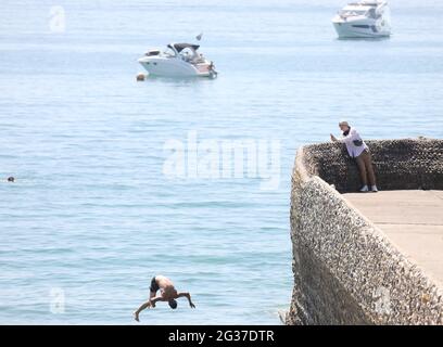 Brighton, Regno Unito. 14 Giugno 2021. Un cercatore di brivido fa un rovesciamento indietro sopra il muro dell'inguine e nel mare mentre la temperatura aumenta sulla costa meridionale. Credit: James Boardman/Alamy Live News Foto Stock