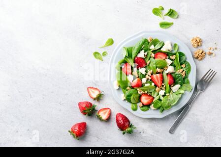 Insalata estiva di fragole con spinaci, noci e formaggio di capra servita su un piatto, vista dall'alto, sfondo grigio in cemento, spazio per testi o disegni Foto Stock