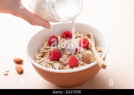 Versare il latte in muesli di avena. Colazione salutare cereali, farinata d'avena, con mandorle e lamponi Foto Stock