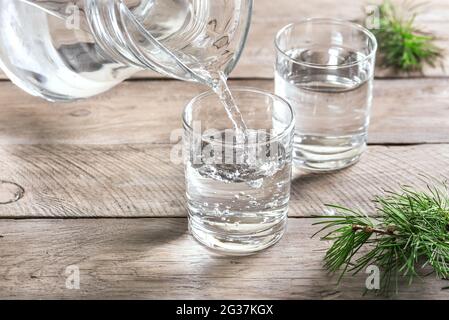Versare l'acqua nel bicchiere. Bicchiere d'acqua su tavolo di legno, fuoco selettivo, primo piano. Acqua purificata limpida per bevande. Foto Stock