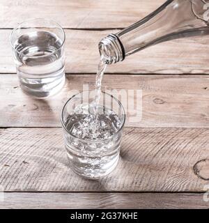 Versare l'acqua nel bicchiere. Bicchiere d'acqua su tavola di legno, fuoco selettivo. Acqua purificata limpida per bevande. Foto Stock